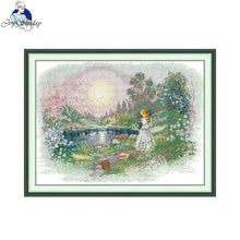 Load image into Gallery viewer, Framed cross-stitch artwork of a woman in a garden with flowers and a lake.