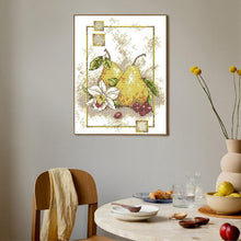 Load image into Gallery viewer, Framed cross-stitch art of a pear on a wall above a dining table with fruit and decor.
