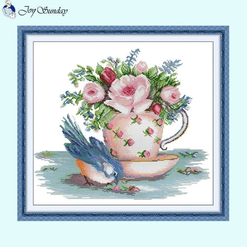 Vintage teacup cross stitch design with songbird and floral patterns on linen fabric.